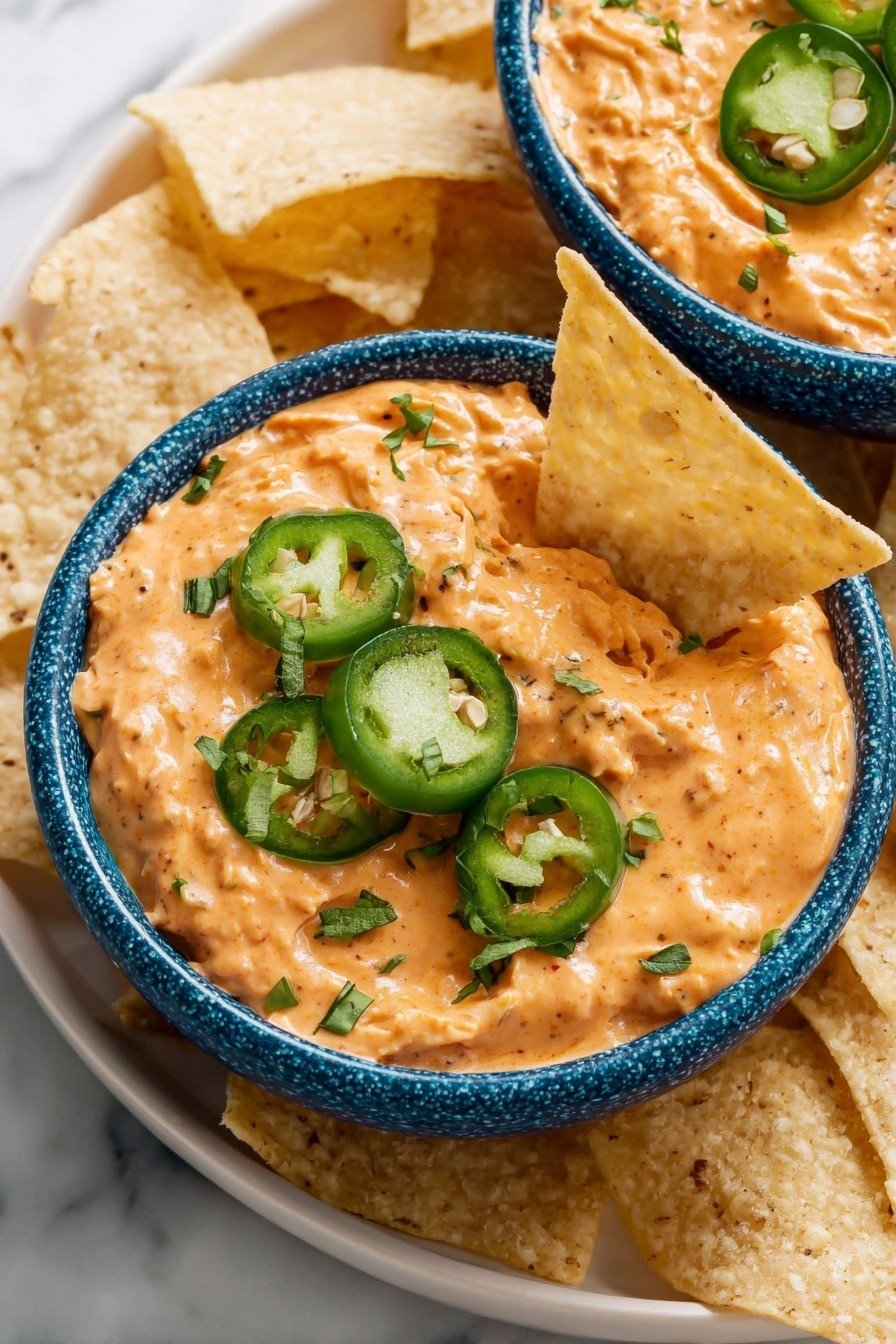 Two bowls of creamy orange dip are placed on a white plate surrounded by light tan tortilla chips. Each bowl is white with a blue rim and filled with a thick orange dip that has small visible chunks, topped with green cilantro leaves scattered across the surface. One bowl has thin green jalapeño slices neatly placed on the right side of the dip. The background is a white marbled surface. photo taken with an iphone --ar 2:3 --v 7