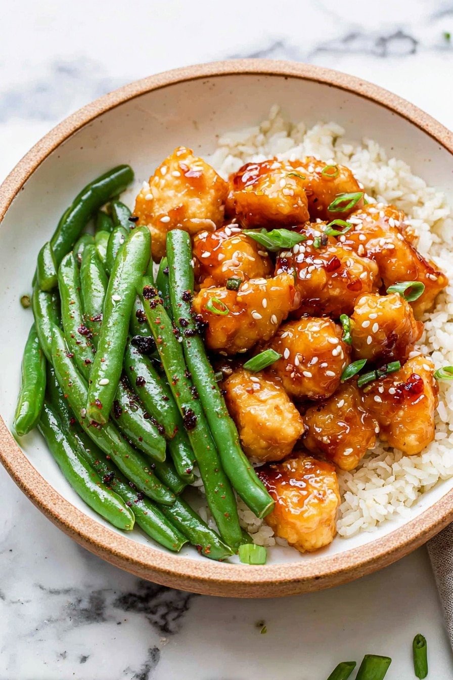 The dish is served in a white bowl with a light brown rim, placed on a white marbled surface. Inside, there are three main layers: at the bottom, white steamed rice spread evenly across half the bowl; on one side, bright green cooked green beans with a shiny texture and sprinkled with black pepper; on the other side and center, golden brown pieces of glazed chicken with a shiny, sticky surface, topped with small white sesame seeds and chopped green onions. The colors contrast well, with the vibrant green, white, and warm golden browns. Photo taken with an iphone --ar 2:3 --v 7