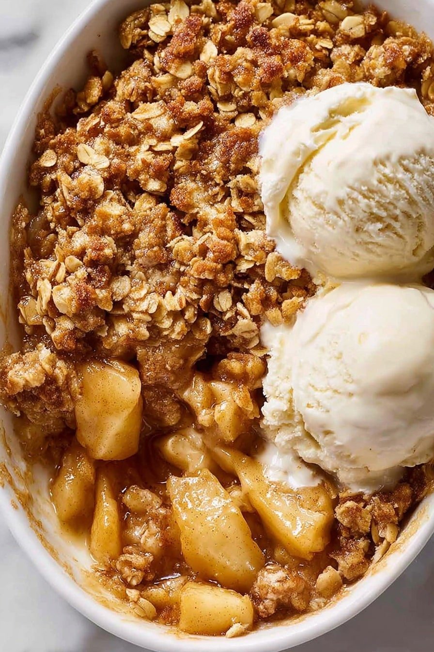 A white oval dish filled with a warm apple crumble topped with a thick layer of golden brown oat and nut crumble that looks crispy and rough in texture. Two scoops of creamy white ice cream melt slightly on top, blending into the crumble. A spoon scoops out a portion from the bottom right, revealing soft, cooked apple pieces with a shiny, light golden color and thick sauce underneath the crumb layer. The dish sits on a white marbled surface with a soft natural light. Photo taken with an iphone --ar 2:3 --v 7