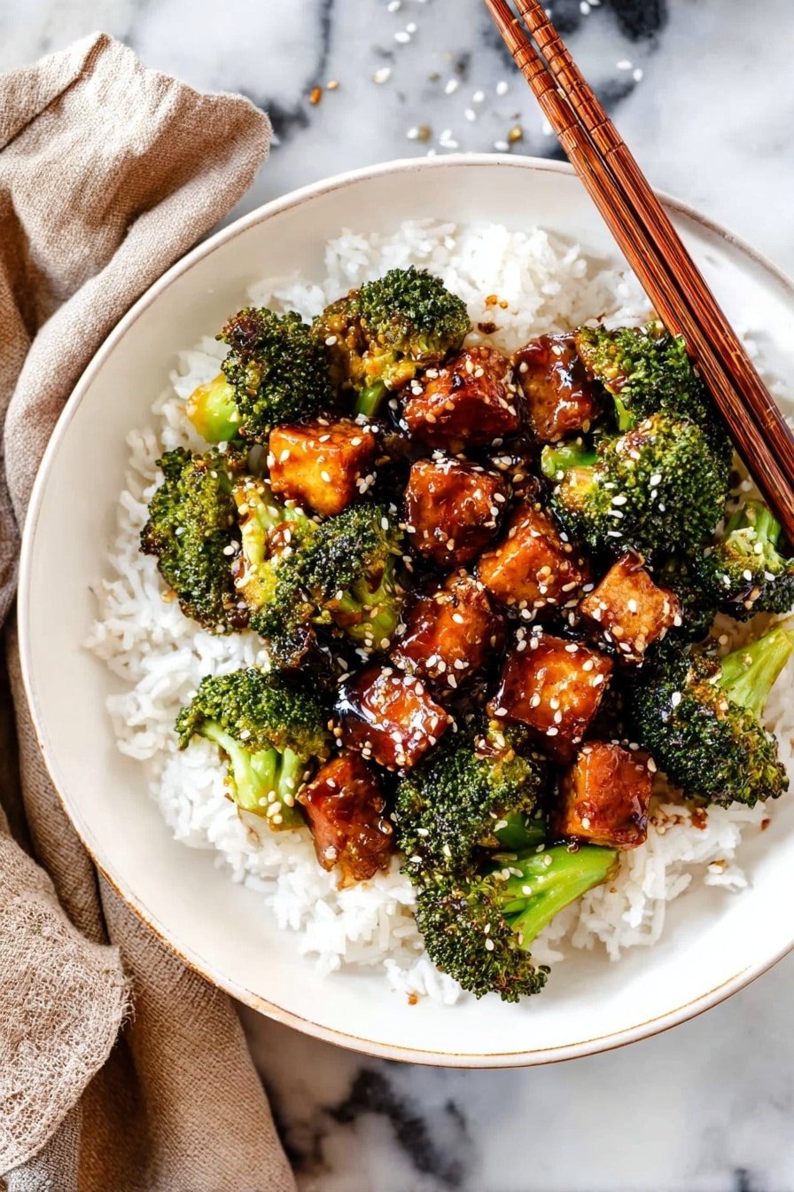 A close-up image shows many small broccoli florets and cubed pieces of brown glazed tofu mixed together. The broccoli is bright green with a fresh texture, and the tofu has a shiny, caramelized surface. White sesame seeds are sprinkled on top, adding a slight contrast and texture. A wooden spatula is seen partially stirring the mix. The dish is in a white bowl, placed on a white marbled surface. Photo taken with an iphone --ar 2:3 --v 7