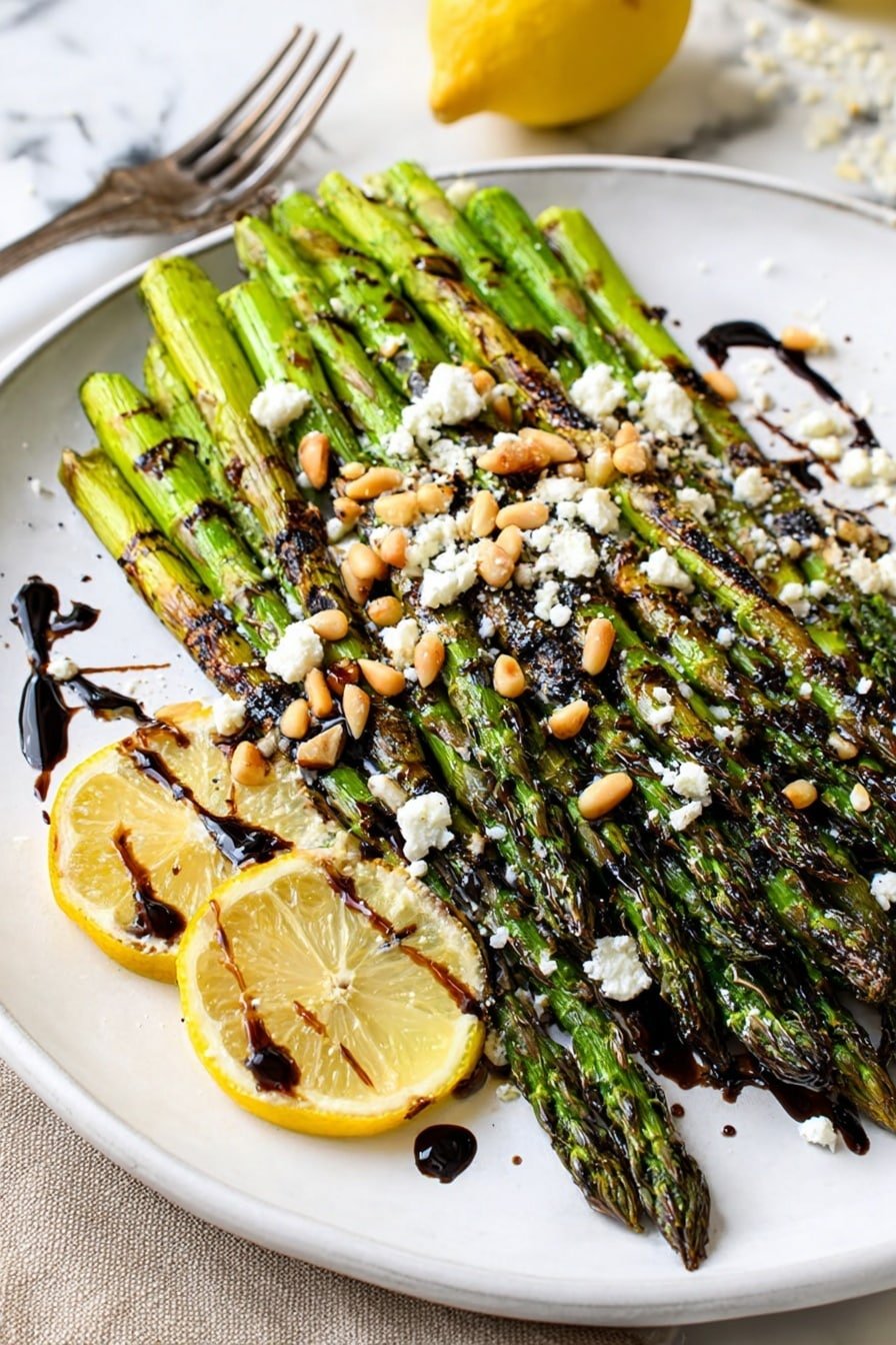A white plate holds a neat pile of grilled green asparagus spears with slight char marks, giving a textured look. The asparagus is topped with scattered white crumbly cheese and light tan pine nuts. Around the asparagus, there are two lemon slices placed on the plate's side, adding a bright yellow contrast. The dish is finished with dark balsamic glaze drizzled over the asparagus and plate. A silver fork lies at the back near the lemon slices on a white marbled surface. Photo taken with an iphone --ar 2:3 --v 7