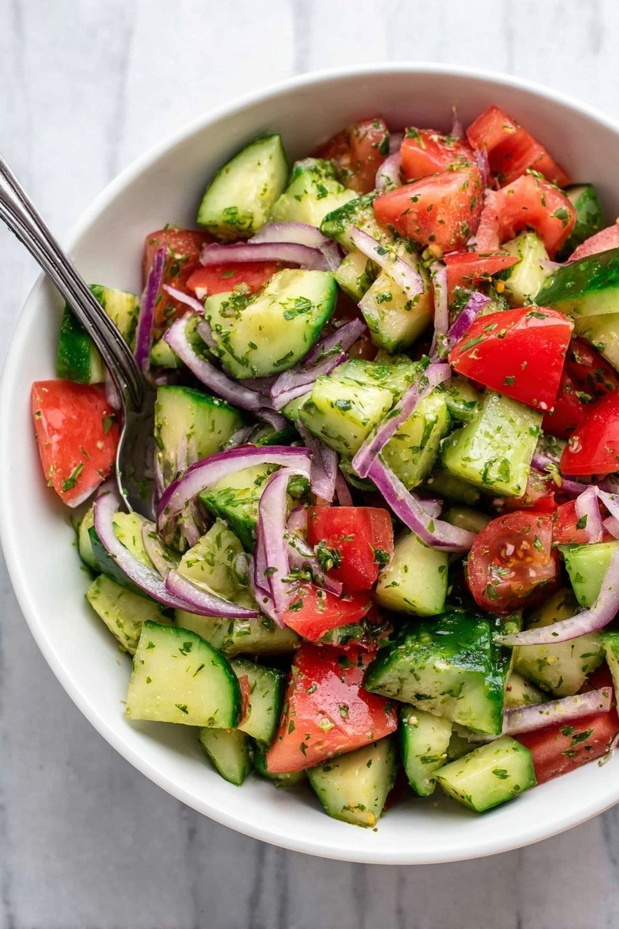 The image shows a white bowl filled with a fresh salad made of three main layers: on the bottom, there are bright green cucumber chunks with dark green skin and light green flesh, in the middle, there are red tomato pieces with soft textures, and on top, thin rings of purple onion are scattered throughout. The salad is mixed with small green herb flakes that add a fine textured layer all over the vegetables. A metal spoon is partly inside the bowl, resting on the mixture on a white marbled surface. Photo taken with an iphone --ar 2:3 --v 7