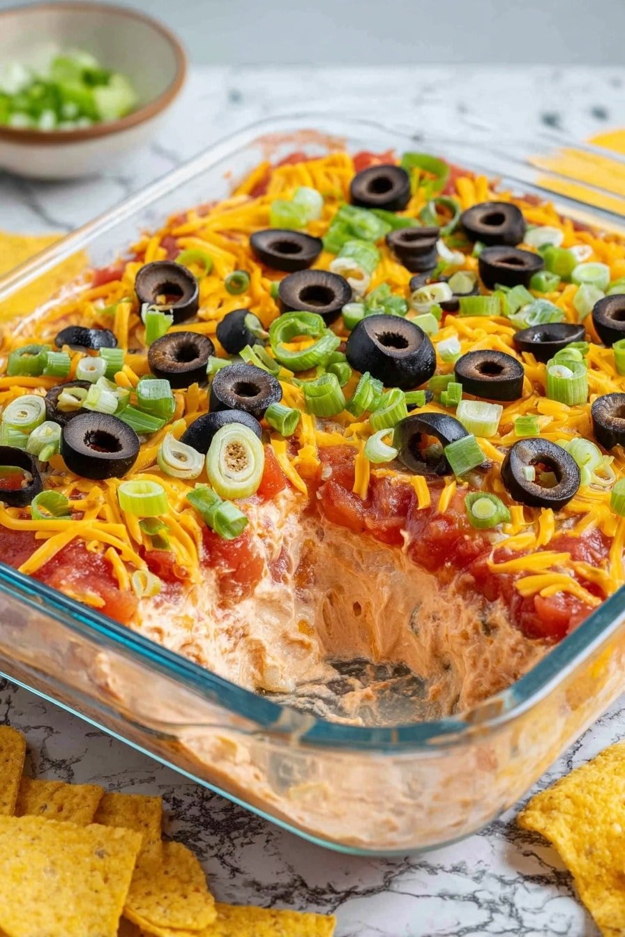 The image shows a clear glass square dish with three visible layers of a dip. The bottom layer is light brown with a smooth texture, the middle layer is bright red tomato salsa with some green peppers, and the top layer is shredded orange cheddar cheese covered with sliced black olives and chopped green onions scattered evenly on top. A scoop is missing from one corner, revealing all the layers clearly. The dish sits on a white marbled surface with some yellow tortilla chips nearby. Photo taken with an iphone --ar 2:3 --v 7