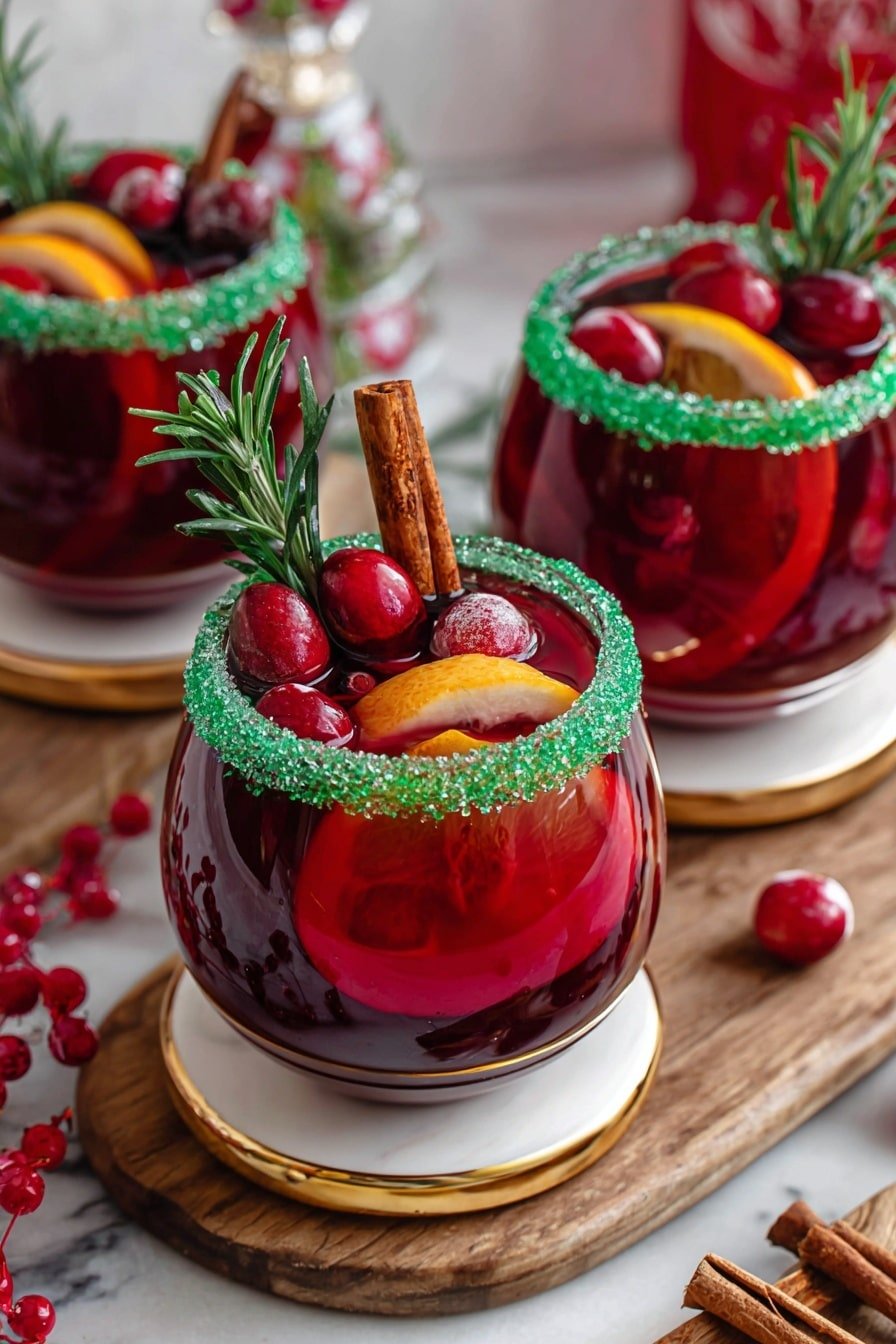 The image shows three round glasses filled with deep red liquid, each glass standing on a white coaster with a gold rim. The drink has several visible layers inside with slices of orange and red fruit floating, giving a mix of orange and red colors. The rim of each glass is coated with bright green sugar crystals, creating a textured bright green ring. On top of the drink, there are small red berries, a sprig of fresh green rosemary, and a brown cinnamon stick standing upright. The glasses are placed on a wooden board on a white marbled surface, with some cinnamon sticks, red berries, and green festive decorations scattered around. Photo taken with an iphone --ar 2:3 --v 7