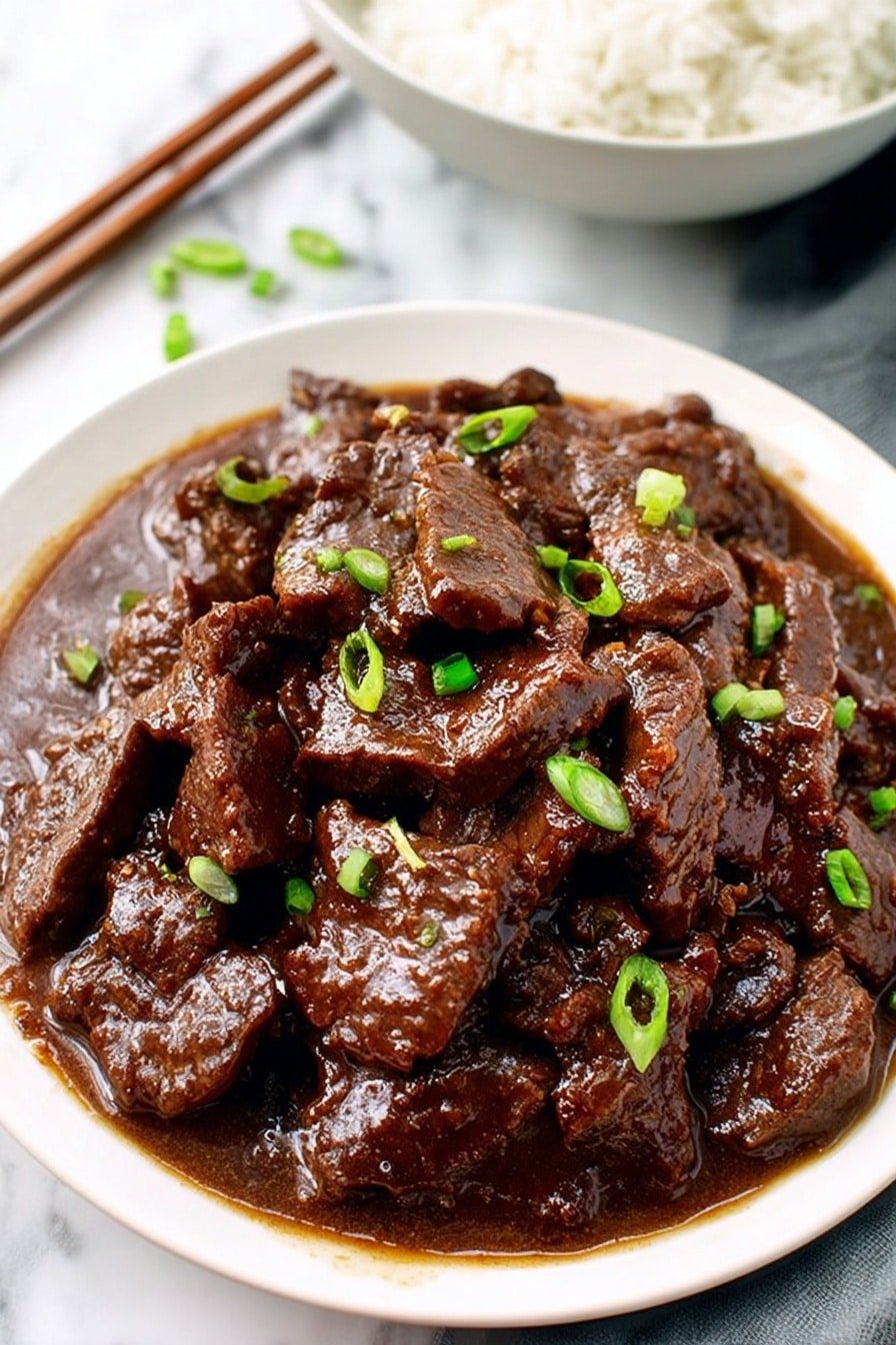 A white plate filled with several thick slices of dark brown beef in a rich, glossy brown sauce that coats the meat evenly. Small bright green pieces of chopped green onion are sprinkled on top, adding color contrast. The plate sits on a white marbled surface, and in the top left corner, a white bowl filled with white rice is partially visible with a pair of brown chopsticks resting on it. photo taken with an iphone --ar 2:3 --v 7