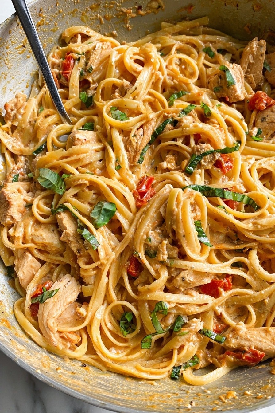 The image shows a close-up of creamy pasta in a white bowl on a white marbled surface. The pasta is long and thick, coated in a light orange sauce with visible specks of herbs and spices. Mixed in are slices of cooked chicken pieces with a light brown color and small pieces of bright green basil leaves scattered on top. There are also small red tomato pieces placed on the pasta. A utensil with sauce and bits is partially visible on the left side of the bowl. The overall texture looks creamy and rich, with ingredients well blended together. Photo taken with an iphone --ar 2:3 --v 7