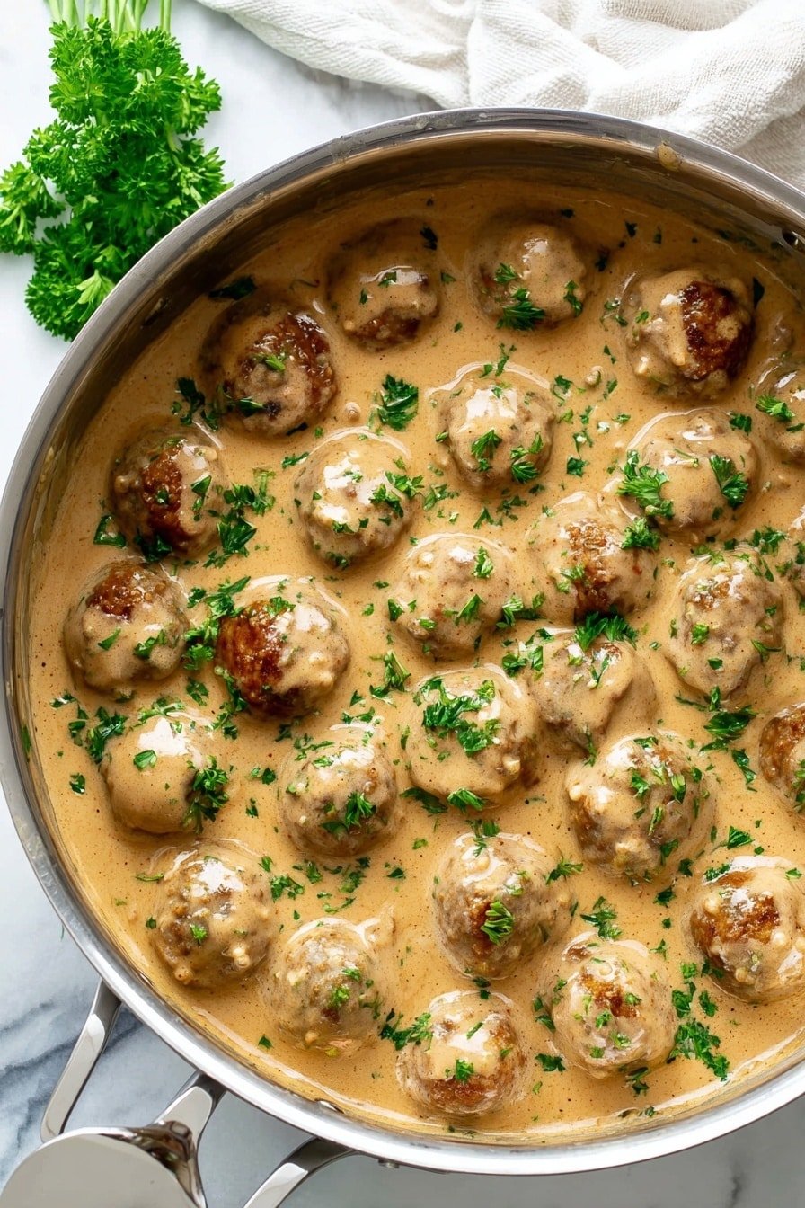 A metal pot filled with about twenty round meatballs, all covered in a thick, creamy light brown sauce with a smooth texture. The meatballs are browned and partially visible through the sauce. Small pieces of fresh green parsley are sprinkled evenly on top, adding a fresh pop of color. The pot is placed on a white marbled surface, with a white cloth partially visible in the background and a sprig of parsley lying next to the pot. Photo taken with an iphone --ar 2:3 --v 7
