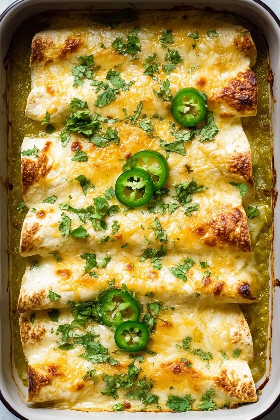 A baking dish filled with five rolled tortillas laid out side by side in a single layer, covered with melted golden cheese that is slightly browned on top. The dish has a green sauce base visible around the edges, with fresh green cilantro leaves scattered evenly across the top along with several slices of green jalapeño pepper placed among the cheese and tortillas. The texture shows a mix of smooth melted cheese and the soft tortillas under it. The photograph is taken on a white marbled surface. photo taken with an iphone --ar 2:3 --v 7