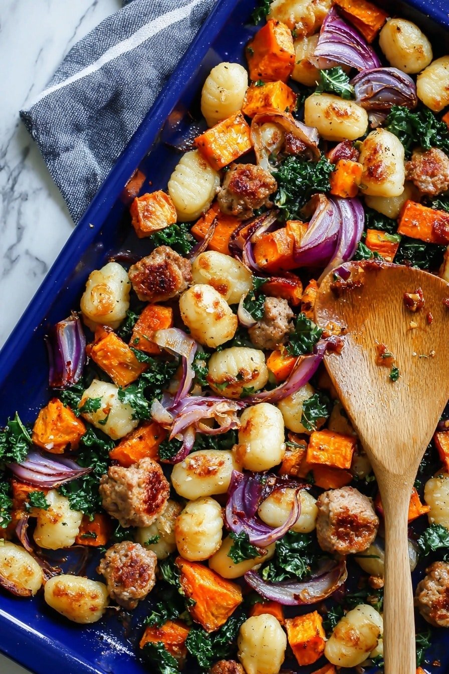 The image shows a close-up of a blue baking tray filled with roasted gnocchi, sausage pieces, diced orange sweet potatoes, red onion slices, and green kale leaves scattered throughout. The gnocchi is plump and golden, some with light char marks. The sausage chunks have a browned, slightly crispy texture. The sweet potatoes are cubed and tender with a vibrant orange color. The red onion slices are soft, slightly translucent with some edges browned. The kale leaves are wilted but still green. A wooden spatula is placed among the food inside the tray. The tray is set on a white marbled surface. photo taken with an iphone --ar 2:3 --v 7