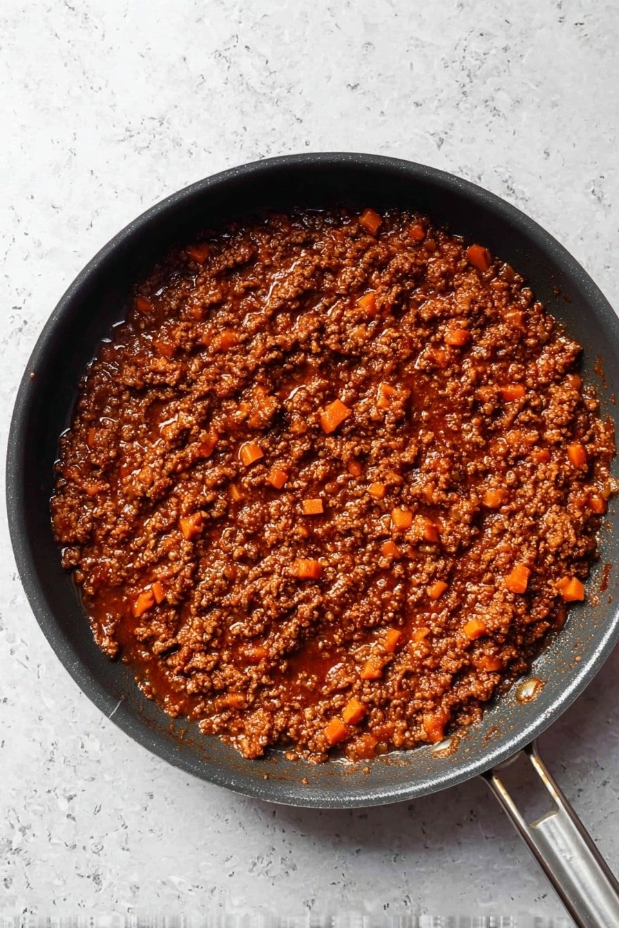 A top view of a black pan filled with a thick layer of rich, dark brown meat sauce mixed with small diced orange carrots; the sauce looks chunky and saucy with a slightly oily shine, sitting on a white marbled surface, with the pan handle extending to the right side of the image photo taken with an iphone --ar 2:3 --v 7