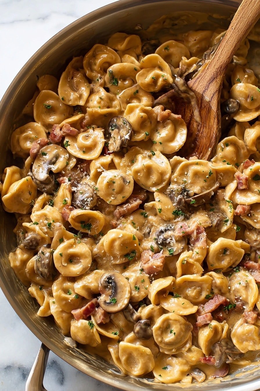 The image shows a close-up of creamy pasta inside a metal pan on a white marbled surface. The pasta is shaped like small, round discs with a slightly curved edge, and it is covered in a rich, light brown sauce. Mixed throughout are small pieces of thinly sliced mushrooms in dark brown and light beige shades, and bits of pinkish bacon. The sauce is smooth and thick, giving the pasta a shiny look. Small green herb flakes are sprinkled on top, adding a fresh touch. A wooden spoon is partially buried in the pasta on the right side of the pan. Photo taken with an iphone --ar 2:3 --v 7