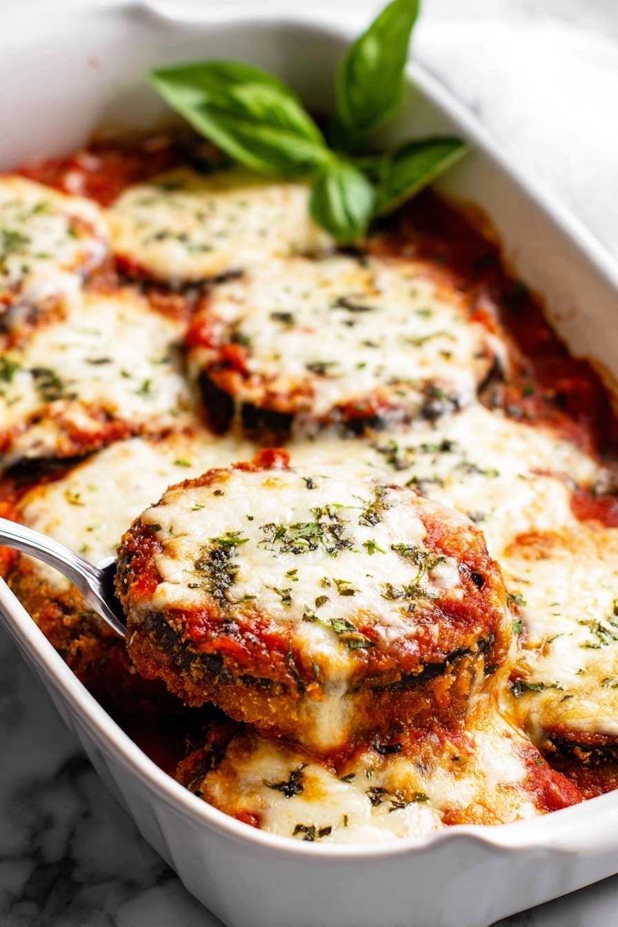A white baking dish filled with several round slices of eggplant layered in three clear layers: bottom is a golden-brown fried crust, middle is bright red tomato sauce, and top is thick, melted white cheese that is bubbly and slightly browned, sprinkled with green herbs. There is a fresh green basil leaf garnish on one side and a spoon inside the dish lifting a cheesy eggplant slice. The dish rests on a white marbled surface. photo taken with an iphone --ar 2:3 --v 7