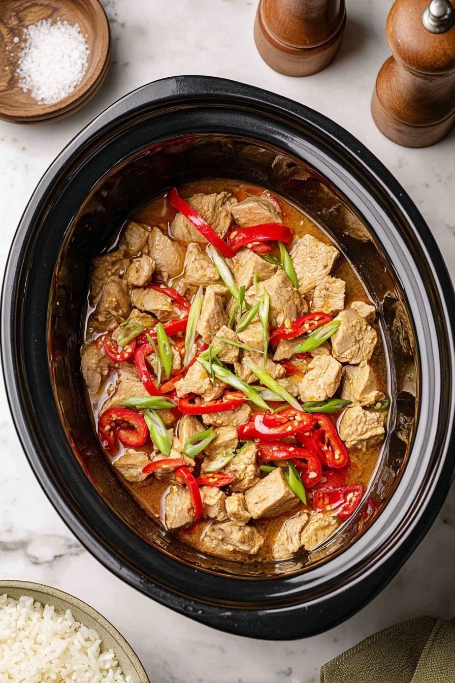 In the image, there is a black slow cooker filled with a dish that has three main layers: the bottom layer is a thin light brown sauce, the middle layer consists of chunks of light tan meat, and the top layer is a mix of bright red bell pepper pieces, thin red chili rings, and green scallion stalks scattered on top. The slow cooker sits on a white marbled surface, with a wooden pepper grinder and a small bowl of coarse salt near the top left corner, and a woman's hand holding a white plate with cooked rice at the bottom left. Photo taken with an iphone --ar 2:3 --v 7