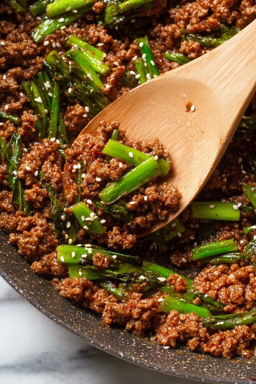 The image shows a close-up of browned ground meat cooked in a pan, mixed with pieces of vibrant green spring onions. The meat looks juicy and slightly oily, with a rich brown color from the sauce. Small white sesame seeds are sprinkled evenly across the meat and onions, adding texture and contrast. A wooden spoon with a smooth texture is lifting a small portion of the meat and green onions, highlighting the mix of colors and textures. The pan rim is slightly worn and the lighting emphasizes the glossiness of the sauce. The background is a white marbled texture. photo taken with an iphone --ar 2:3 --v 7
