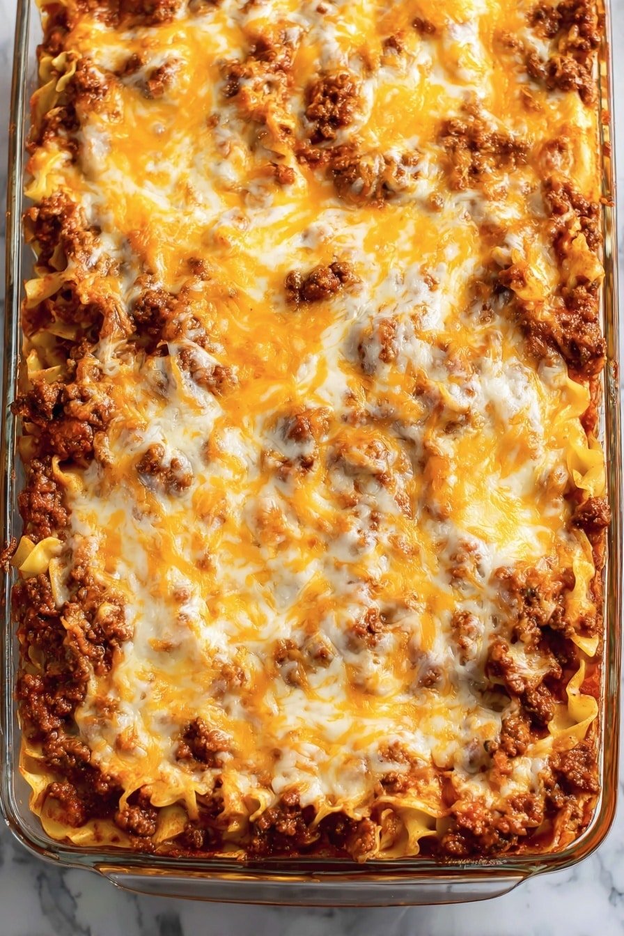 The image shows a clear glass baking dish with one main layer of cooked pasta, covered with a thick layer of browned ground meat mixed in tomato sauce, topped with a bubbly layer of melted orange and white cheese that is spread unevenly across the surface, showing some of the meat sauce underneath. The dish is placed on a white marbled surface. Photo taken with an iphone --ar 2:3 --v 7