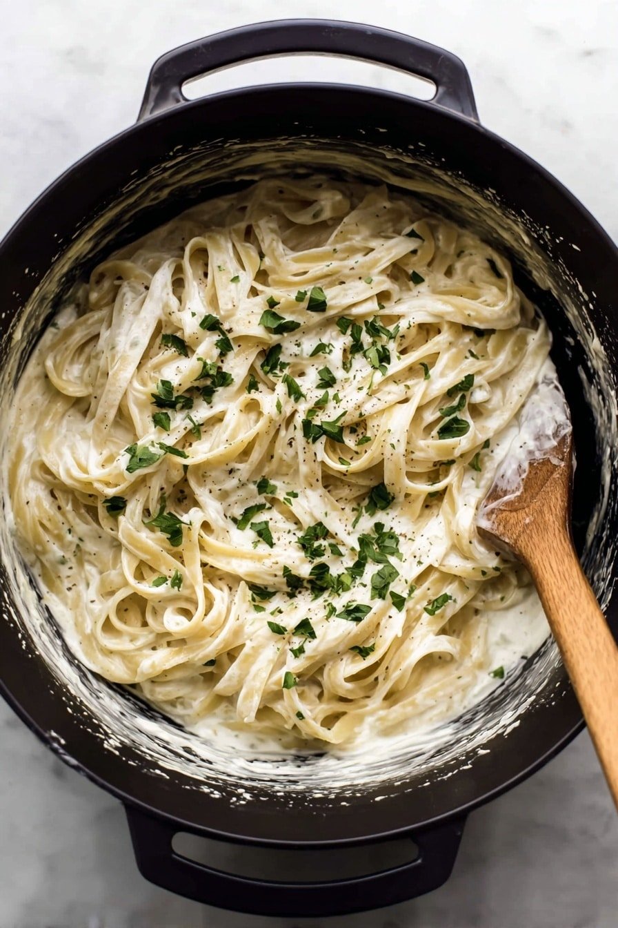 A black pot filled with creamy white fettuccine pasta layered with a smooth, thick sauce that coats the noodles evenly, topped with scattered bright green chopped parsley, creating a fresh contrast. The pasta strands are long and flat, twisted slightly, sitting in the center of the pot with some sauce residue on the pot’s sides. A wooden spoon rests on the right edge of the pot, partly covered with sauce. The pot is placed on a white marbled surface. Photo taken with an iphone --ar 2:3 --v 7