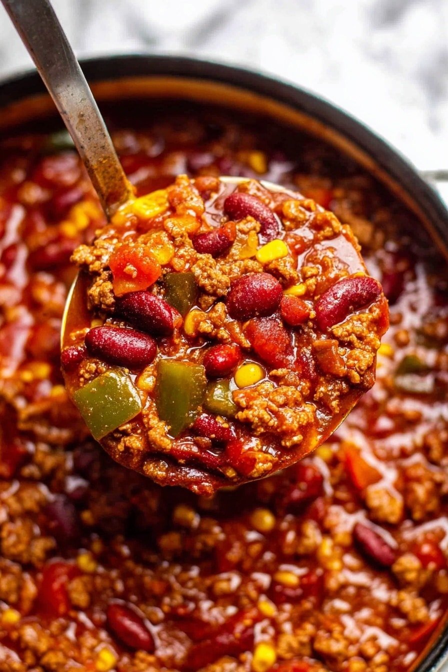 The image shows a close-up of a thick chili stew filled with multiple layers of ingredients. The base layer is a deep red sauce with a glossy, slightly oily texture. Mixed throughout are soft pieces of minced meat that appear brown and finely crumbled. Bright red kidney beans are scattered across the dish, some partly submerged in the sauce. There are also small chunks of green bell peppers and pieces of yellow corn adding pops of color. A metal ladle scoops up a generous portion of the chili, showing the mix of textures and colors close-up. The background has a white marbled texture. Photo taken with an iphone --ar 2:3 --v 7