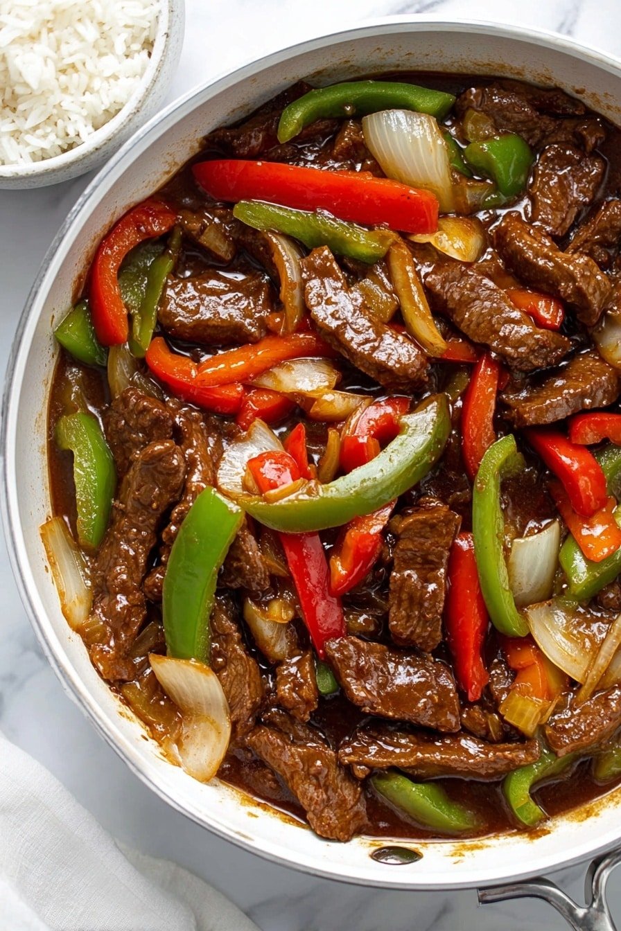 The image shows a shiny white pan filled with stir-fried beef strips covered in a glossy brown sauce. Mixed throughout the beef are slices of green and red bell peppers and chunks of cooked onions, all glistening with sauce. The beef pieces are the darkest layer, thick and juicy, while the bell peppers and onions add bright red, green, and pale yellow colors, creating a colorful contrast. To the left side of the pan, a bowl with plain white rice is slightly visible. The background surface is a white marbled texture. photo taken with an iphone --ar 2:3 --v 7