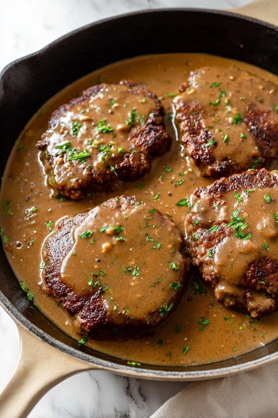 This image shows three thick brown meat patties partially covered in smooth light brown gravy with darker brown spots, all sitting inside a black cast iron pan with a beige handle. The gravy contains small bits and is garnished with finely chopped bright green herbs scattered over the meat and sauce. The pan rests on a white marbled surface with a soft white cloth nearby. The lighting is natural, highlighting the glossy texture of the gravy and the slightly crispy edges of the meat. photo taken with an iphone --ar 2:3 --v 7