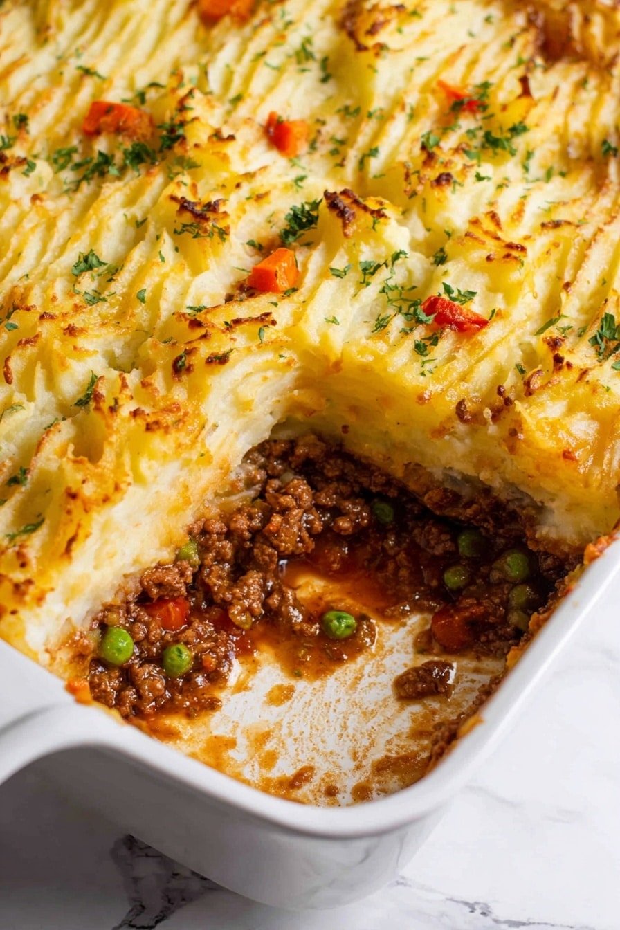 A white rectangular baking dish filled with a layered shepherd’s pie. The top layer is golden brown mashed potatoes with small ridges and peaks, slightly browned and garnished with bits of chopped parsley and small orange carrot pieces. Below, there is a thick, rich meat sauce layer with visible ground meat, green peas, and small red pieces of vegetables mixed in a savory brown gravy. The pie is partially scooped out from one corner, showing the distinct two layers and some sauce residue on the dish sides. The background is a white marbled texture. Photo taken with an iphone --ar 2:3 --v 7