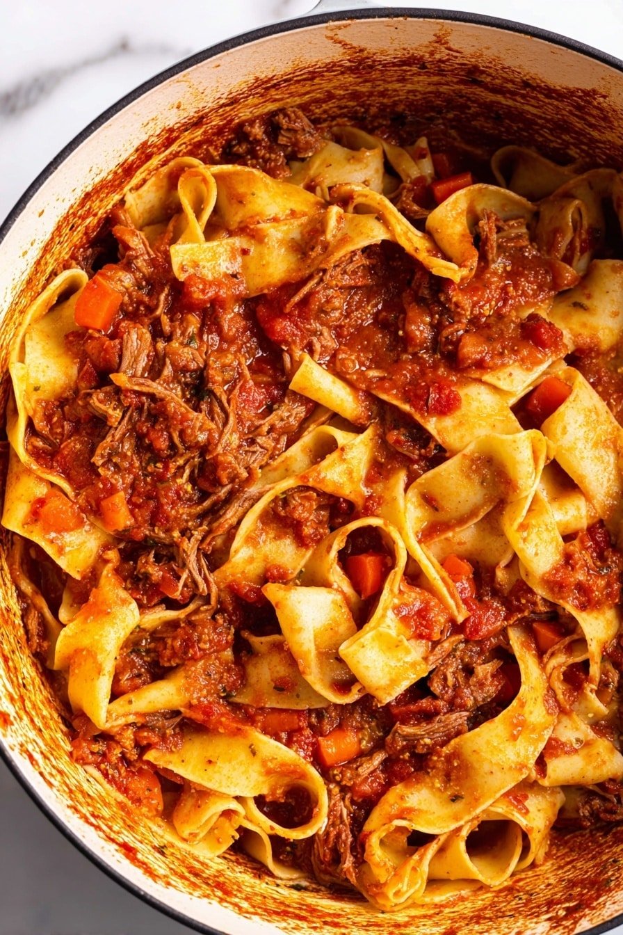 This image shows a close-up of a large pot filled with wide, flat pasta noodles, mixed with a rich, chunky red tomato sauce. The sauce has visible small pieces of carrots and bits of tender, shredded brown meat scattered throughout. The noodles are a warm yellow color, soft and folded in different directions, coated well with the sauce. The inside rim of the pot shows a ring of cooked sauce residue in dark brown and reddish tones. The background is a white marbled texture. Photo taken with an iphone --ar 2:3 --v 7