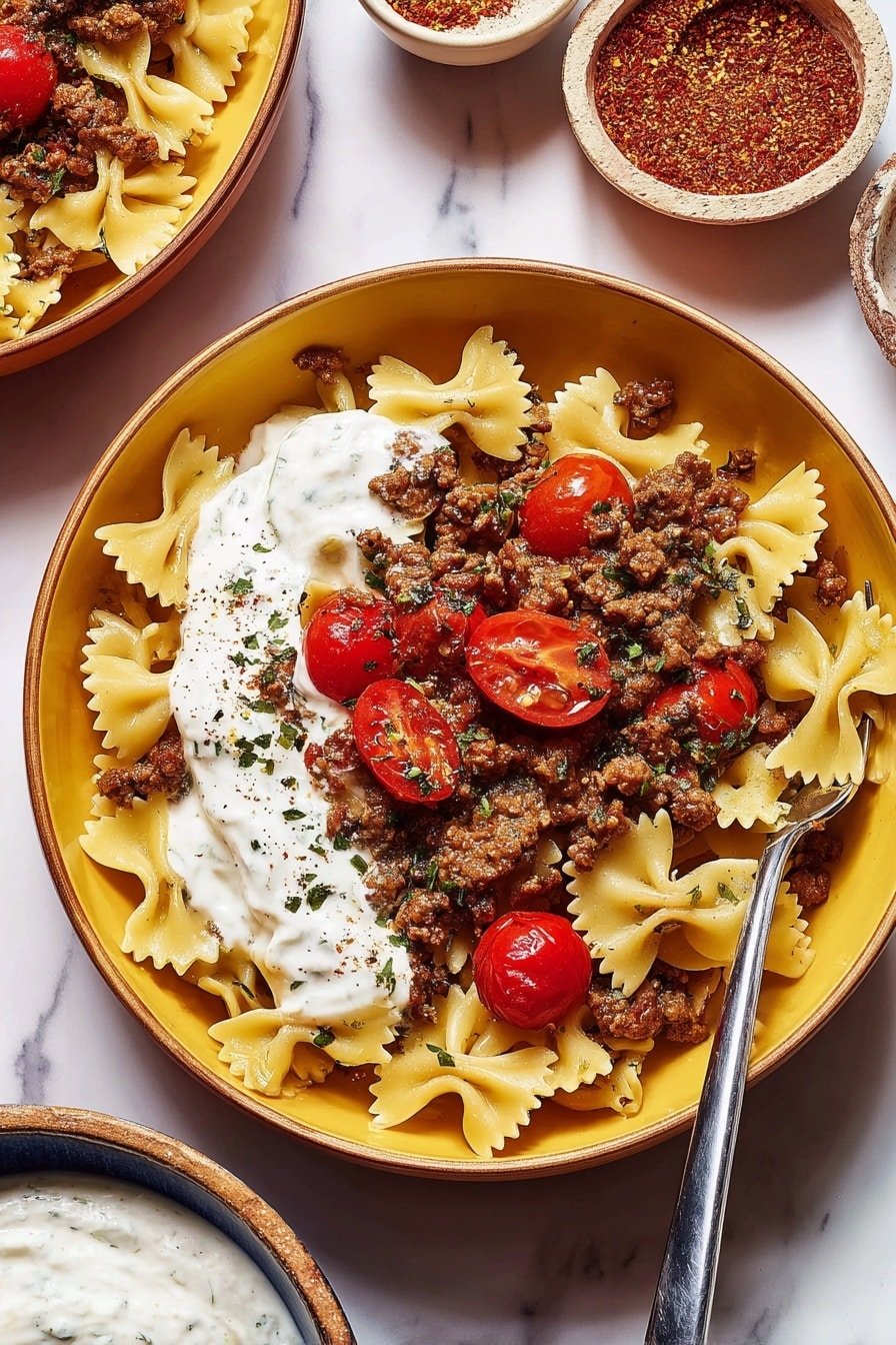 The image shows a round yellow bowl filled with three main layers: the bottom layer is light yellow farfalle pasta spread evenly, the middle layer is thick dollops of white creamy sauce, and the top layer is a mix of browned ground meat with small onion pieces and bright red cherry tomato halves sprinkled with green dried herbs. A fork rests on the right side of the bowl, partially in the pasta. In the background, there are smaller bowls with a red spice and a white sauce, all placed on a white marbled surface. Photo taken with an iphone --ar 2:3 --v 7