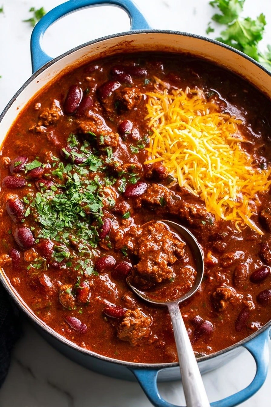 A blue pot filled with thick chili showing large chunks of browned meat and dark red kidney beans mixed in a rich, deep red sauce. On one side of the chili, there is a small pile of shredded yellow cheese and a dollop of white sour cream. Fresh green chopped herbs are sprinkled lightly over the top. A silver ladle is placed inside the pot with its handle resting on the edge. The pot sits on a white marbled surface with some green leafy herbs visible near the top right. Photo taken with an iphone --ar 2:3 --v 7