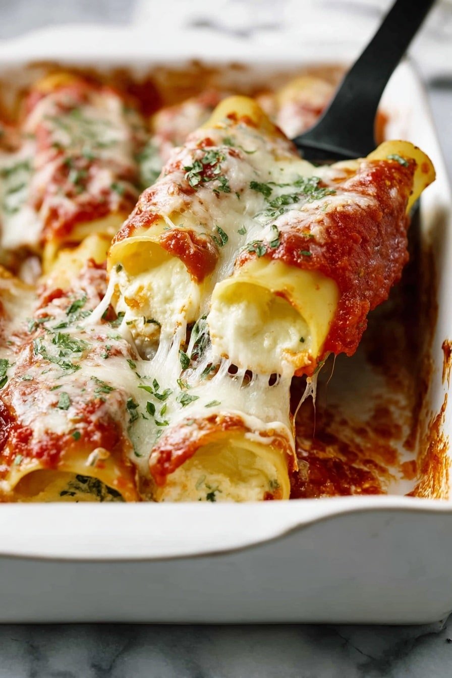 A white baking dish filled with several large rolled pasta tubes standing upright, each stuffed with creamy white cheese and topped with thick red tomato sauce and melted mozzarella cheese that stretches as one is lifted by a black spatula. The cheese layer is bubbly and slightly browned in spots, sprinkled with fresh green herbs, all set on a white marbled surface. Photo taken with an iphone --ar 2:3 --v 7