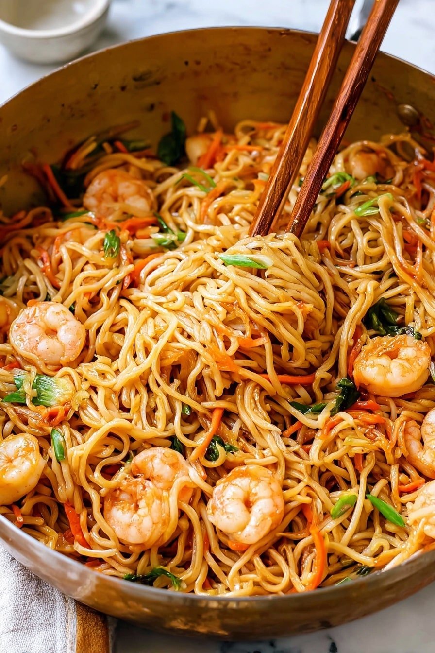 A close-up of a large round metal pan filled with cooked noodles mixed with pink shrimp, thin orange carrot strips, and small green onion pieces. The noodles are light brown and look soft, tangled around each other in one layer, with shrimp and vegetables evenly spread throughout. A pair of wooden chopsticks lifts a portion of the noodles from the middle of the pan, showing the mix of ingredients clearly. The pan is set on a white marbled surface, and in the background, there is a blurry white container. Photo taken with an iphone --ar 2:3 --v 7