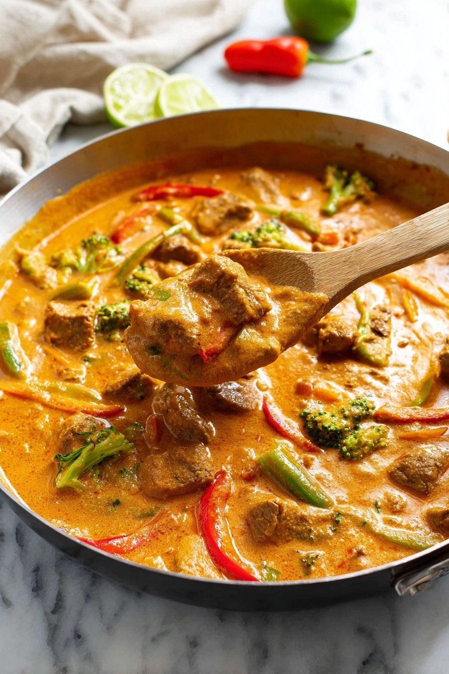 A black pan filled with a thick orange curry sauce that has many chunks of brown meat and pieces of green broccoli and red bell pepper scattered throughout. A woman's hand with red polished nails is holding a silver spoon scooping the curry, showing the creamy texture and colorful mix in the sauce. The pan is placed on a white marbled surface with some small peppers and a green lime in the background, along with a white cloth and a small clear bowl with chopped herbs. The scene is bright and warm, highlighting the rich colors and textures of the curry. photo taken with an iphone --ar 2:3 --v 7