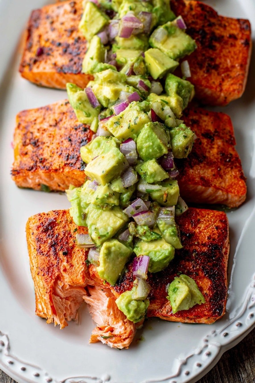The image shows two pieces of cooked salmon fillets placed side by side on a white plate, with a grilled texture visible on their orange-pink surface showing some blackened spots. On top of the salmon, there is a chunky avocado mixture made of light green avocado chunks and small purple-red pieces of red onion, creating a colorful contrast with the fish. The salmon is flaked slightly in one corner, revealing its soft, moist inside. The background surface is a white marbled texture. Photo taken with an iphone --ar 2:3 --v 7