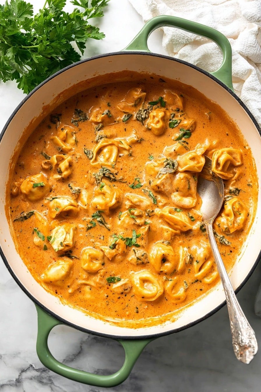A white pot with green handles is filled with a creamy orange sauce mixed with small pasta pieces shaped like tortellini and chunks of meat, spread evenly throughout the sauce. Small green herbs are scattered on top, adding texture and color contrast. A silver ladle rests inside the pot, partially covered in the sauce. The pot is placed on a white marbled surface with some fresh green parsley leaves visible to the left and a white cloth to the upper right photo taken with an iphone --ar 2:3 --v 7