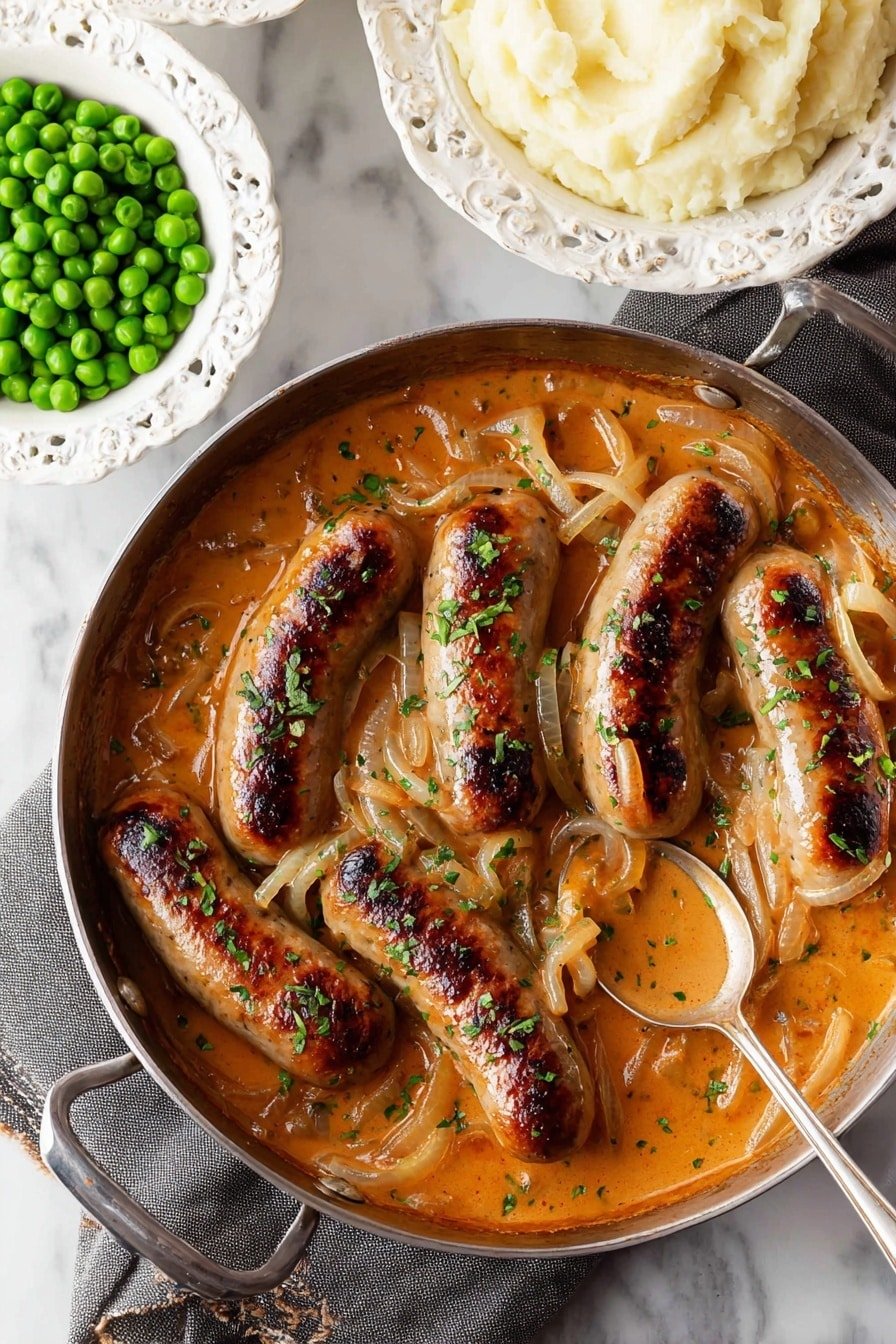 In the center, a black cast iron pan holds six browned sausages in a rich, orange-brown creamy sauce with thin slices of translucent onions and sprinkled green herbs on top. The sausages are plump and a few have darker charred stripes. A silver spoon rests in the sauce near the bottom right side of the pan, showing the thick texture of the sauce. In the background, there are two ornate white bowls, one filled with bright green peas and the other with smooth, fluffy off-white mashed potatoes. The whole scene is set on a white marbled texture with a gray cloth under the pan’s handle. photo taken with an iphone --ar 2:3 --v 7