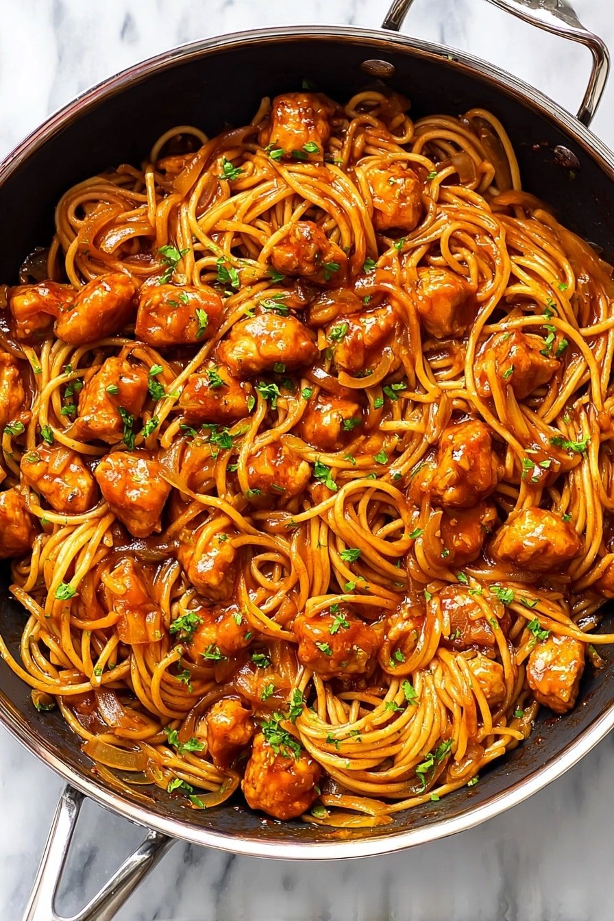 A metal pan filled with spaghetti mixed with medium-sized orange-brown sauce-covered chicken pieces and thin cooked onions, all coated in a glossy, rich reddish-orange sauce. The chicken pieces are scattered evenly throughout the spaghetti noodles, which are intertwined and slightly glossy from the sauce. Small bits of green herbs are sprinkled on top for a touch of color. The pan sits on a white marbled texture. photo taken with an iphone --ar 2:3 --v 7