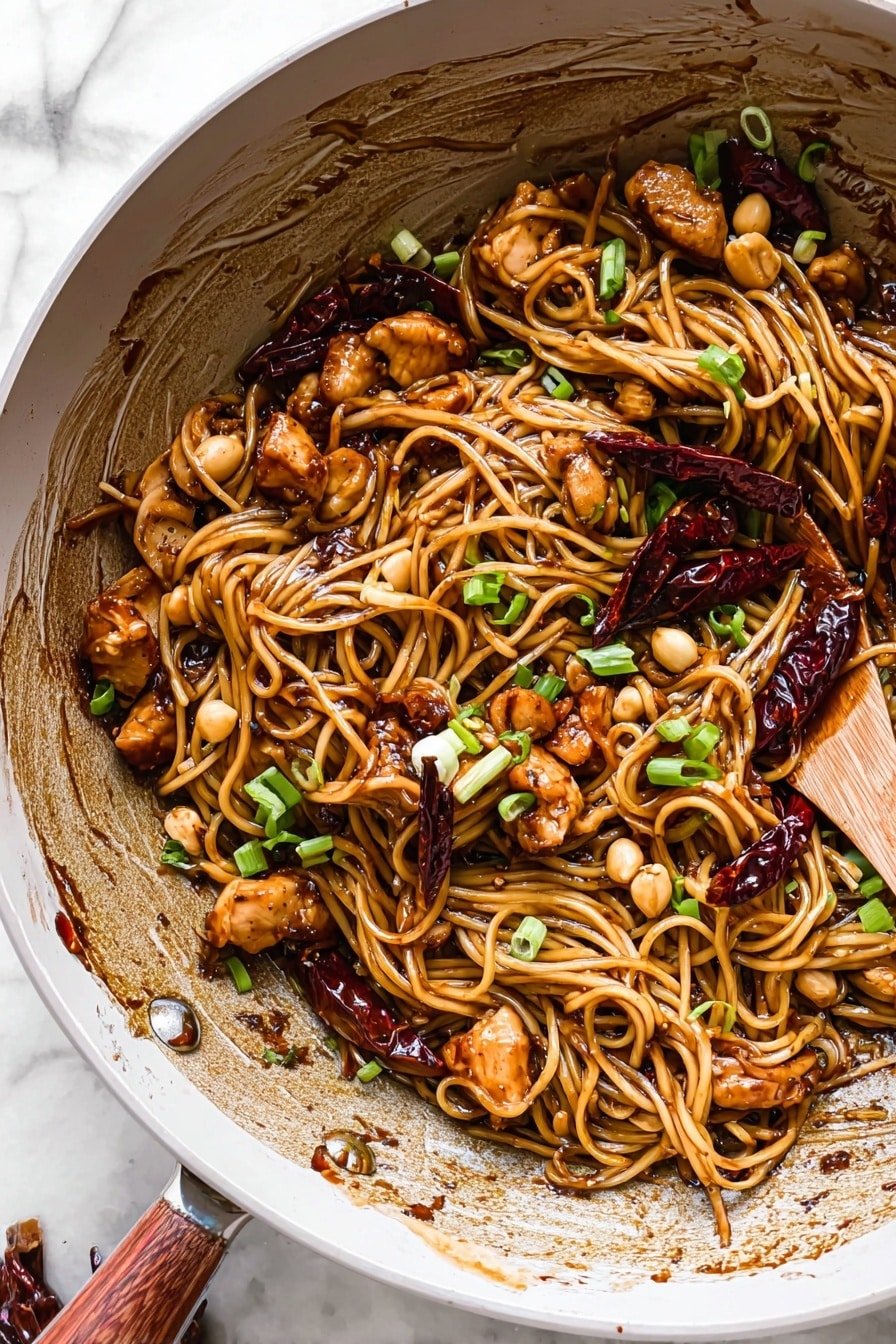 In an ornate white bowl sitting on a white marbled texture, there is a dish with several layers. The base layer is a mix of long, thin noodles coated with a dark brown glossy sauce. Scattered through the noodles are medium-sized light brown chunks of cooked chicken and small tan peanuts. On top, there are several dark red dried chili peppers, and fresh green sliced scallions add a pop of color. A pair of wooden chopsticks held by a woman’s hand is lifting a nest of noodles on the right side of the bowl. The bowl edges have splashes of sauce, showing a rustic, appetizing touch. Photo taken with an iphone --ar 2:3 --v 7