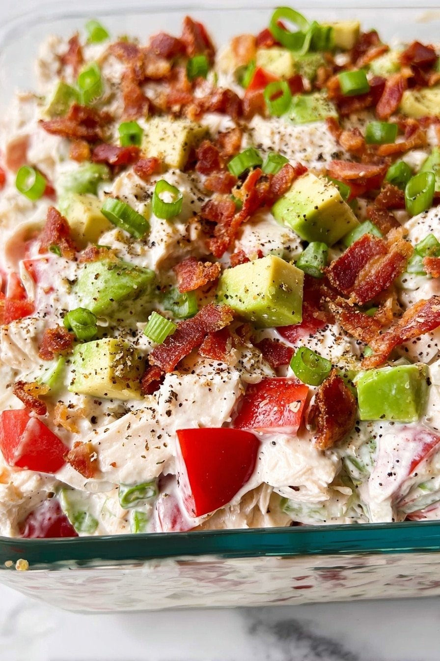 The image shows a close-up of a layered dish in a clear glass container resting on a white marbled surface. The top layer is a mix of creamy white chunks with a soft texture, scattered with bright green avocado cubes, red tomato pieces, and small crispy brown bacon bits. There are also thin slices of green onions spread on top, with a sprinkling of coarse black pepper adding texture and contrast. The colors are fresh and vibrant, with the creamy base layer holding the ingredients together in a colorful, hearty mix. photo taken with an iphone --ar 2:3 --v 7