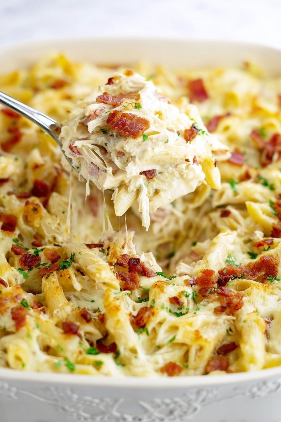 A close-up view of a baked pasta dish inside an ornate white dish, showing creamy white penne pasta mixed with shredded white chicken and sprinkled with small red-brown bacon pieces and chopped green herbs, topped with a layer of melted white cheese that looks soft and slightly stringy, with a metal serving spoon lifting a scoop of the pasta mixture from the dish, all set against a white marbled texture photo taken with an iphone --ar 2:3 --v 7