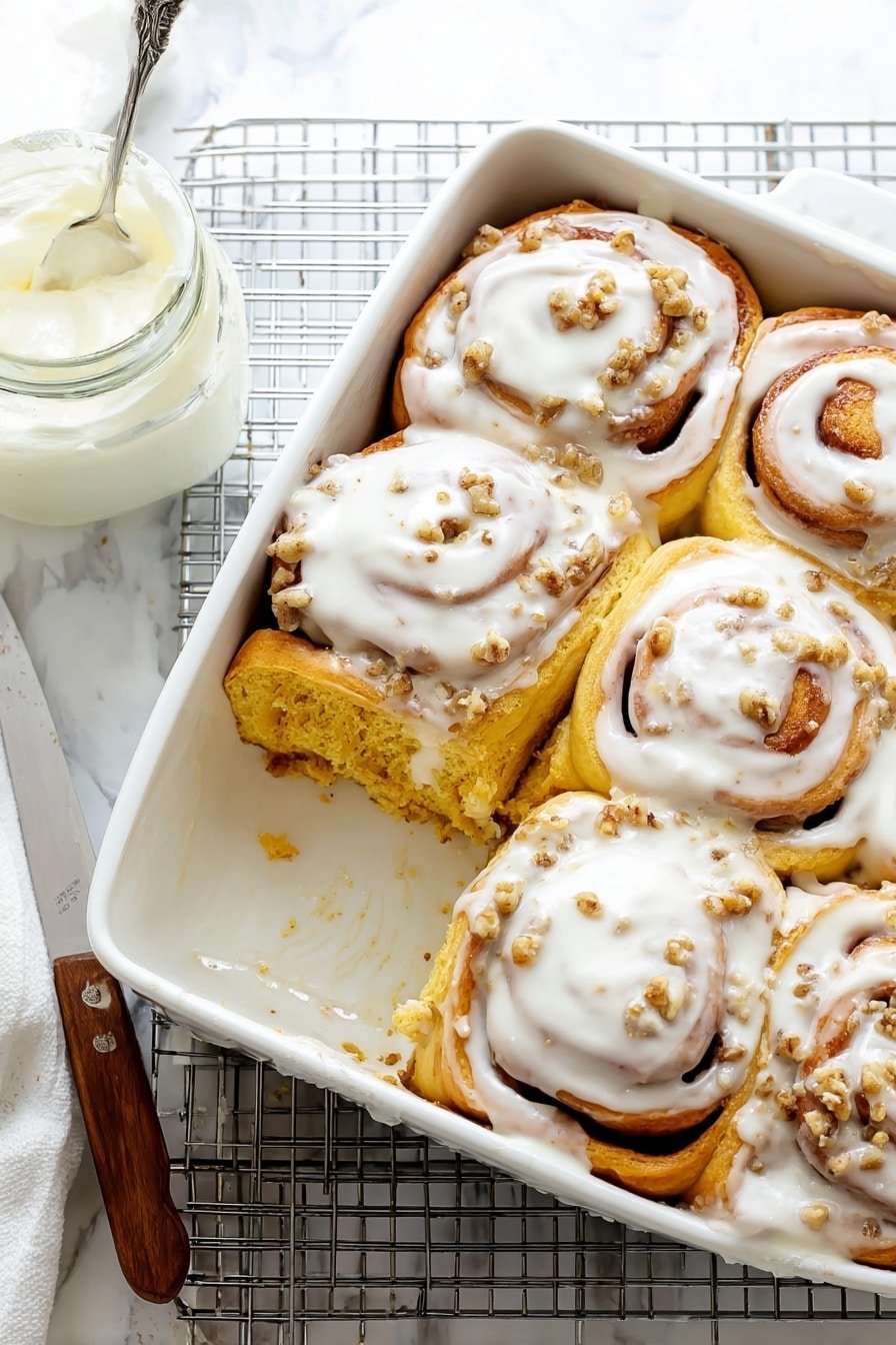 The image shows a white ceramic baking dish with six cinnamon rolls inside, five whole and one piece missing from the bottom left corner. Each cinnamon roll has a golden brown spiral base with thick white icing smoothly spread on top, slightly melting and dripping over the sides. The cinnamon rolls sit closely together, filling the dish. To the left of the baking dish, there is an ornate white plate holding the missing cinnamon roll piece, topped with the same white icing. Below the plate and near the dish, a butter knife with a wooden handle rests on a cooling rack. To the upper left, a small clear glass container holds some of the same white icing. The whole scene rests on a white marbled surface. Photo taken with an iphone --ar 2:3 --v 7