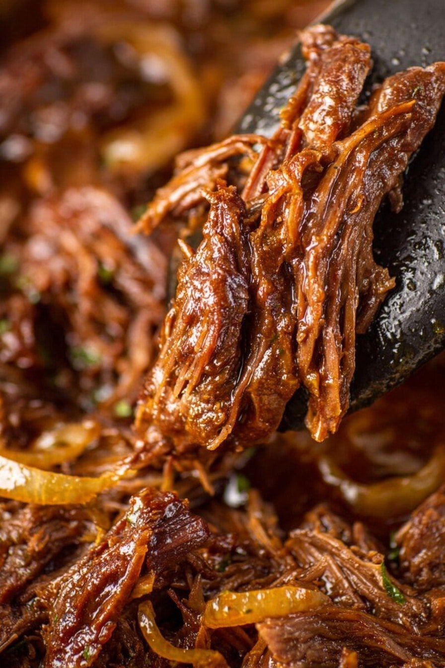 A close-up view shows several pieces of tender, shredded dark brown meat with a glossy coating of thick sauce, held up by a metal spatula on the right side. The meat strands have a fibrous texture and a rich, juicy appearance, with hints of herbs and spices scattered throughout. Below, on a bed of the same saucy shredded meat, there are soft, slightly translucent caramelized onion slices adding a lighter amber color to the deeper browns of the meat. The background has a blurred warm brown tone, emphasizing the glossy, rich textures of the meat in the foreground. Photo taken with an iphone --ar 2:3 --v 7