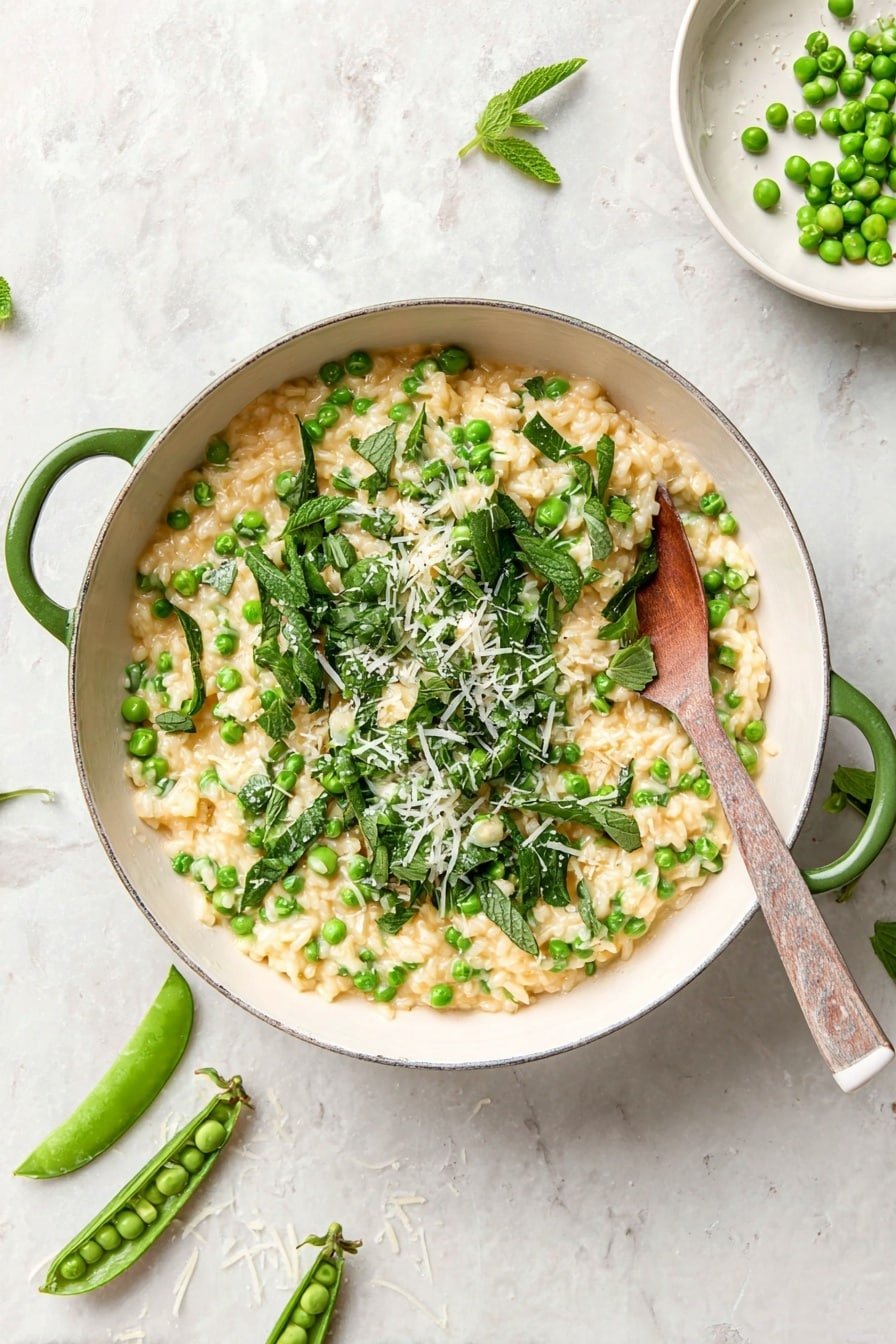 The image shows a white scalloped bowl filled with creamy risotto that is pale yellow in color, mixed evenly with small green peas. On top, there is a layer of fresh green snap peas, some cut open to show peas inside, and scattered fresh mint leaves, giving a bright green contrast. Shredded white cheese is lightly sprinkled over the greens. A silver spoon sits on the right edge of the bowl. Around the bowl, there are extra snap peas, some opened, and a few loose peas and mint leaves scattered on a white marbled surface. Photo taken with an iphone --ar 2:3 --v 7