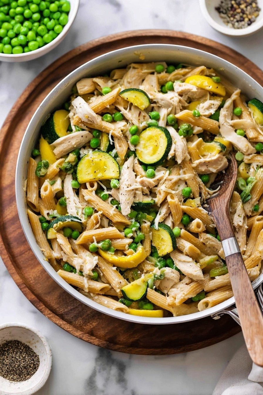 The image shows a white pan filled with a colorful pasta dish. The bottom layer has light brown penne pasta mixed with bright green peas, and slices of yellow and green zucchini scattered throughout. Shredded white chicken pieces are layered evenly on top and mixed into the pasta and vegetables. A wooden spoon with a brown handle rests inside the pan, partially covered by the food. The pan is set on a round wooden board over a white marbled surface. In the background, a bowl filled with more green peas and a small bowl with black pepper are softly focused. photo taken with an iphone --ar 2:3 --v 7