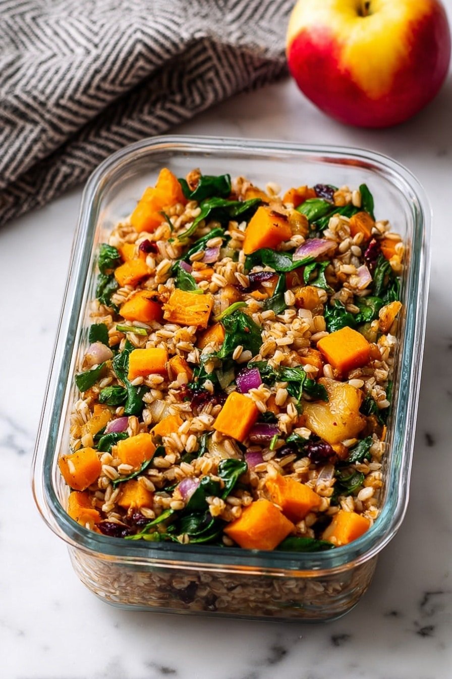 The image shows a clear rectangular glass container filled with a mixed grain salad. The dish has one main layer made up of light brown grains, bright orange cubes of cooked squash or sweet potato, fresh dark green spinach leaves, small orange carrot slices, and bits of red onion. The colors are warm and earthy, with a mix of soft and leafy textures. The container sits on a white marbled surface, next to a red-yellow apple and a gray cloth with a subtle chevron pattern. photo taken with an iphone --ar 2:3 --v 7