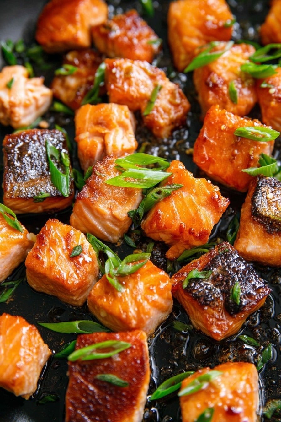 There are many small square pieces of cooked salmon with some pieces having shiny, browned skin on one side. The salmon is a mix of light orange and rich brown with some caramelized textures. Green onion slices, bright green and fresh, are scattered on top of the salmon pieces. The dish is shown close up on a black pan with some oil shining around, and the salmon looks juicy and well cooked. The background has a white marbled texture. photo taken with an iphone --ar 2:3 --v 7