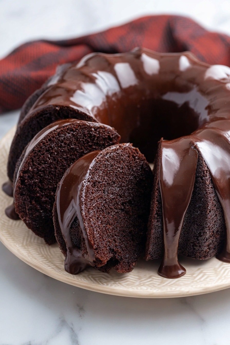 A sliced chocolate bundt cake is shown on a white plate placed on a white marbled surface. The cake has a deep dark brown color with a smooth and glossy chocolate glaze that drips down the sides of the thick, ring-shaped cake. The inside texture looks soft and moist, with the slices fanning out slightly to reveal the rich chocolate crumb inside. Behind the cake, there is a blurred light cloth adding softness to the scene. Photo taken with an iphone --ar 2:3 --v 7