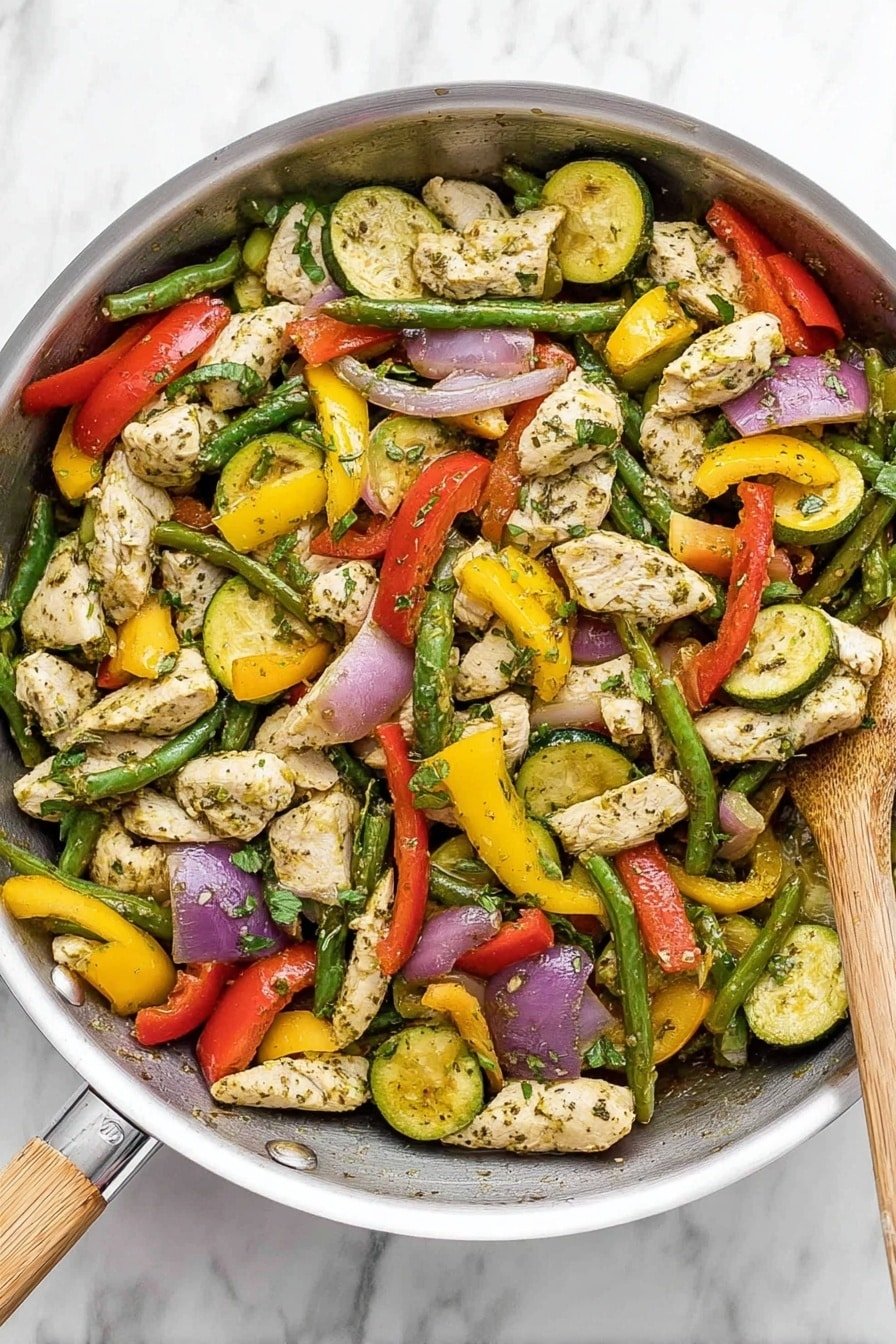 A silver frying pan filled with a colorful stir-fry of cooked sliced chicken pieces that are white with some herbs, mixed with bright green string beans, red bell pepper pieces, yellow squash slices, green zucchini slices, and purple onion slices. The vegetables and chicken are lightly coated with herbs and spices, giving a slightly speckled look, and some fresh green herbs are sprinkled on top. The pan is on a white marbled surface with a black spatula resting on the side of the pan. photo taken with an iphone --ar 2:3 --v 7