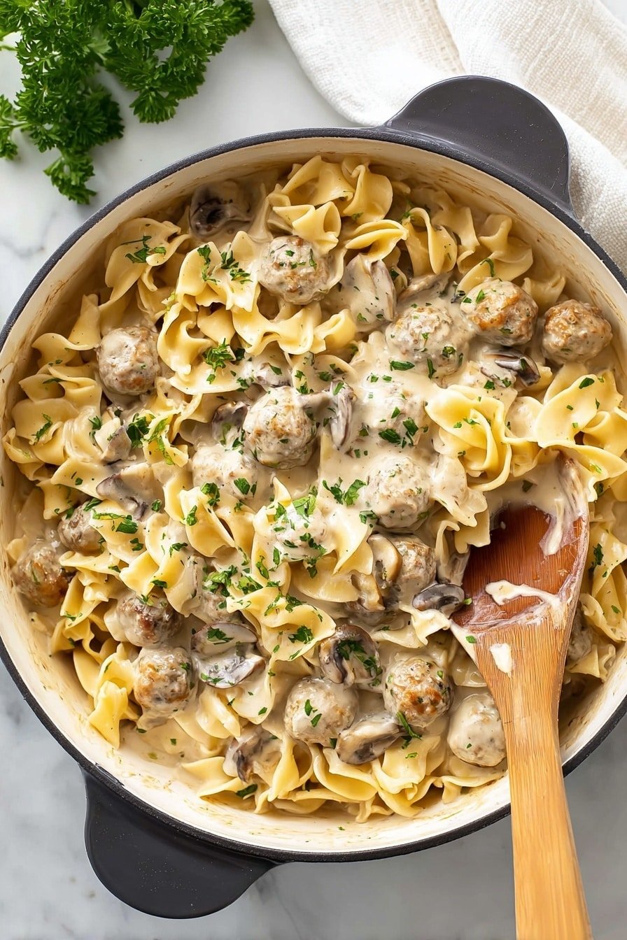 A large black pot with an ornate white inside holds a creamy dish with three main layers: light beige wide egg noodles twisted in shape, small round beige meatballs, and medium brown sliced mushrooms. All the ingredients are covered in a thick creamy white sauce speckled with finely chopped green herbs, likely parsley. A wooden spoon rests inside the pot on the right side, partially covered with sauce. The pot sits on a white marbled surface with a sprig of parsley in the top left corner and a white cloth in the upper right. Photo taken with an iphone --ar 2:3 --v 7