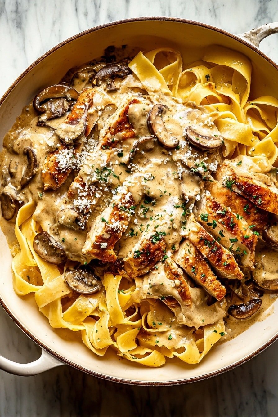 A white bowl holds three main layers: at the bottom, a bed of flat yellow pasta ribbons with a soft, smooth texture, slightly curled and intertwined; above the pasta, browned pieces of grilled chicken with a light golden crust are laid out; on top, creamy beige sauce covers the chicken and pasta, thick and rich in texture, with sliced brown mushrooms embedded in it. The sauce is sprinkled with small bits of green herbs and tiny white cheese granules. A silver fork is placed in the bowl, partly resting on the pasta and chicken. The bowl sits on a white marbled surface. Photo taken with an iphone --ar 2:3 --v 7