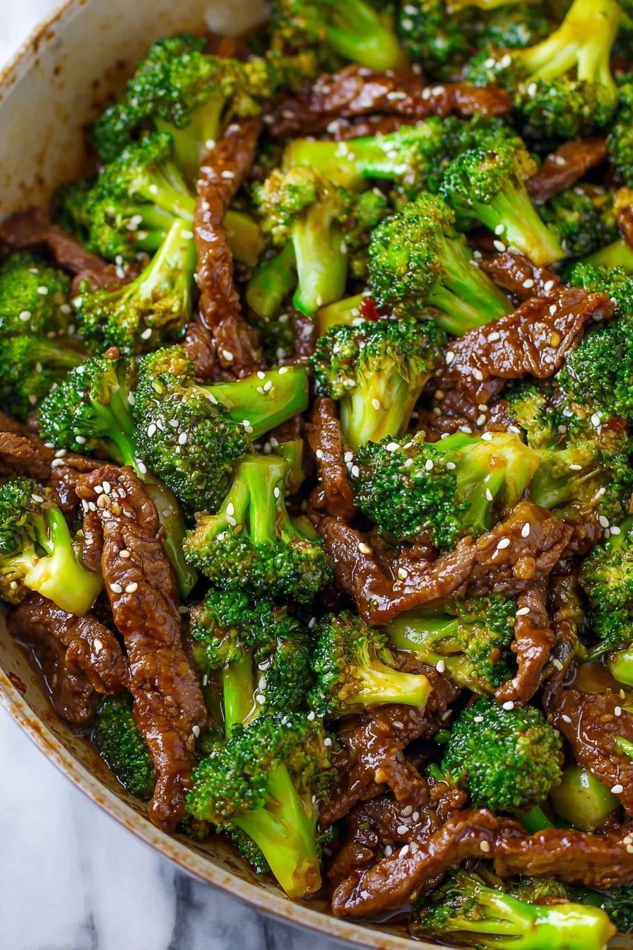 The image shows a close-up view of a stir fry dish in a white pan. The dish has two main layers: the first layer consists of bright green broccoli florets with a slightly shiny texture from the sauce, spread evenly throughout the pan. The second layer includes thinly sliced brown beef pieces coated in a rich, dark brown sauce, mixed among the broccoli. Small white sesame seeds are sprinkled on top, adding a delicate texture contrast. The overall look is glossy and vibrant, with the green and brown colors creating a balanced mix. The background is a white marbled surface. Photo taken with an iphone --ar 2:3 --v 7