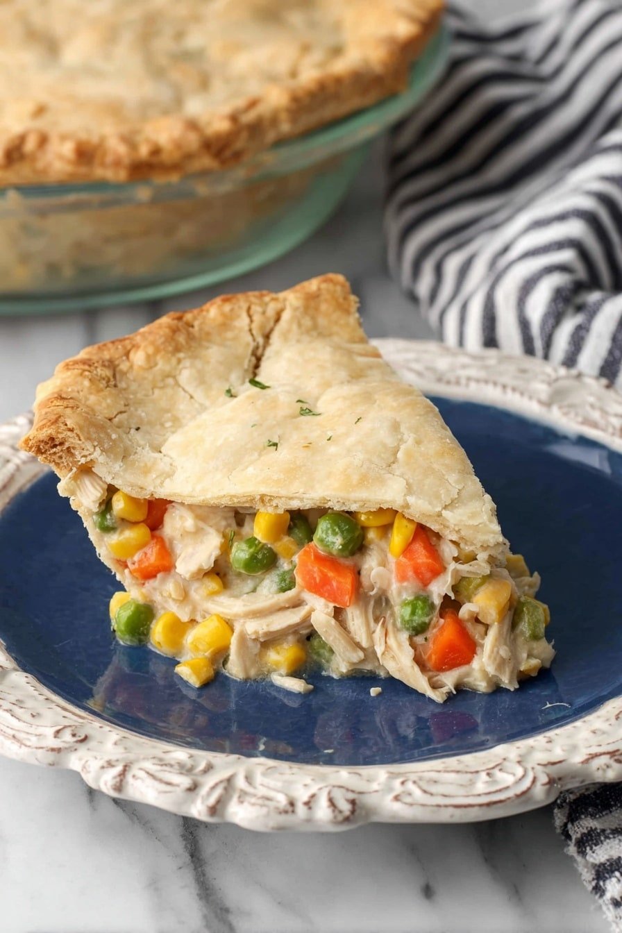 A slice of golden-brown pie with a flaky crust sits on an ornate white plate with a deep blue center. The pie has two layers: the top layer is a smooth, light beige crust with slight cracks, and the bottom layer is filled with a creamy mixture of bright orange carrot cubes, green peas, yellow corn kernels, and shredded white meat in a white sauce. The filling slightly spills over the crust edges, showing the colorful vegetables clearly. In the background, a glass pie dish with the rest of the pie is partially visible on a white marbled surface with a black and white striped cloth nearby. photo taken with an iphone --ar 2:3 --v 7